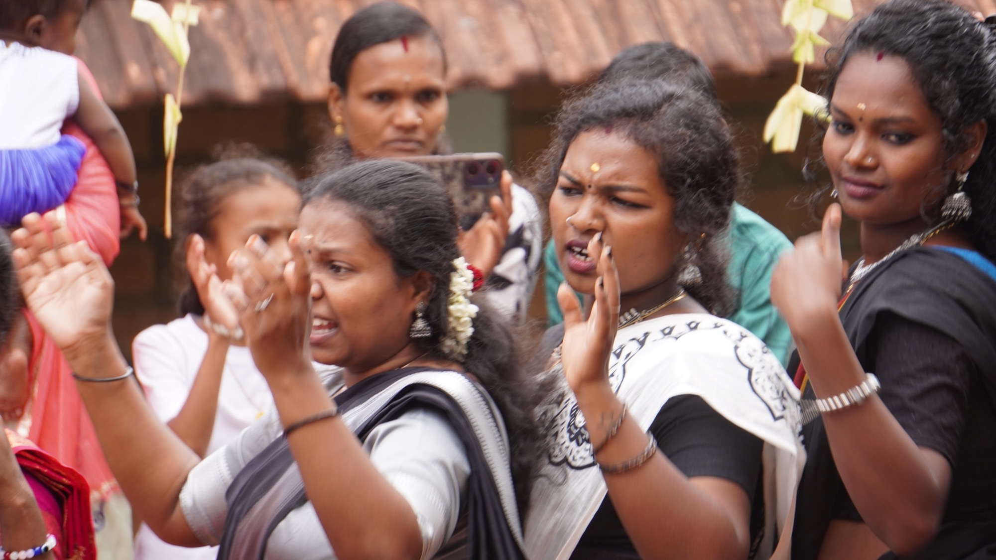 Adivasi women dancing and clapping in a row at the celebration, animated expressions