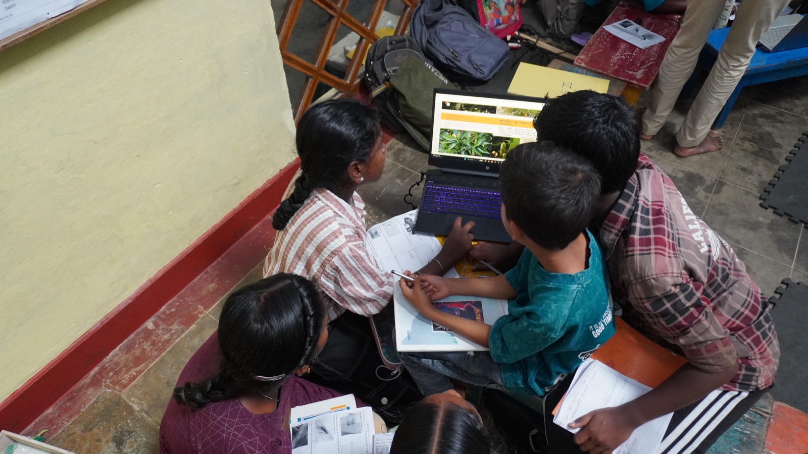 Adivasi youth gathered around a laptop, studying together