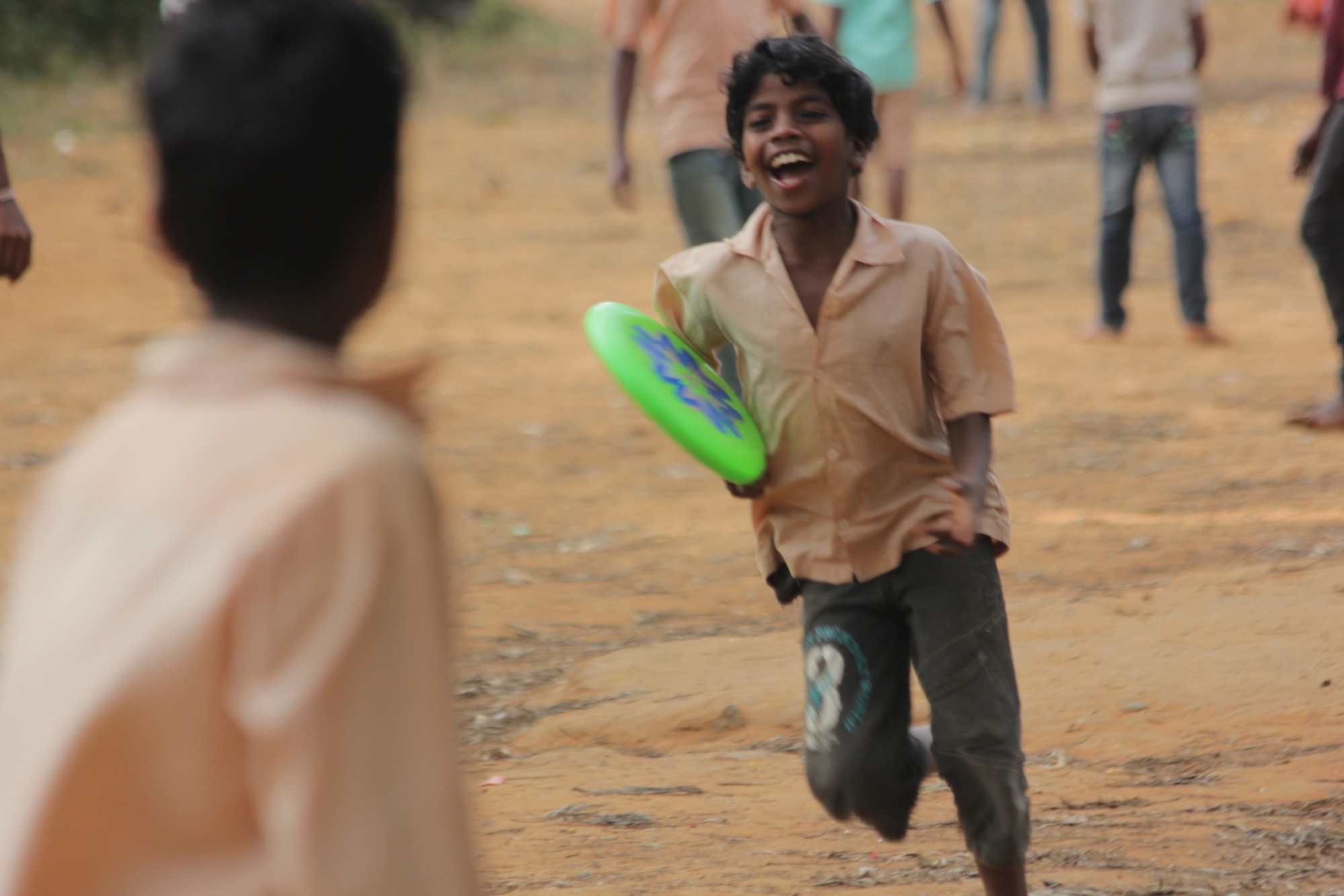 Boy laughing as he runs with a green frisbee during outdoor play