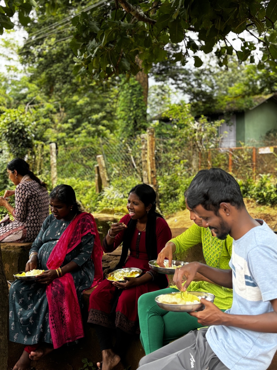Candid of four young Adivasi adults eating a meal together on a wall outdoors, laughing