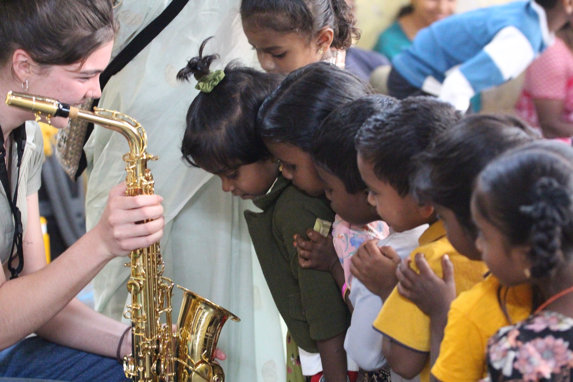 Children leaning in to look at a saxophone held by a visiting musician