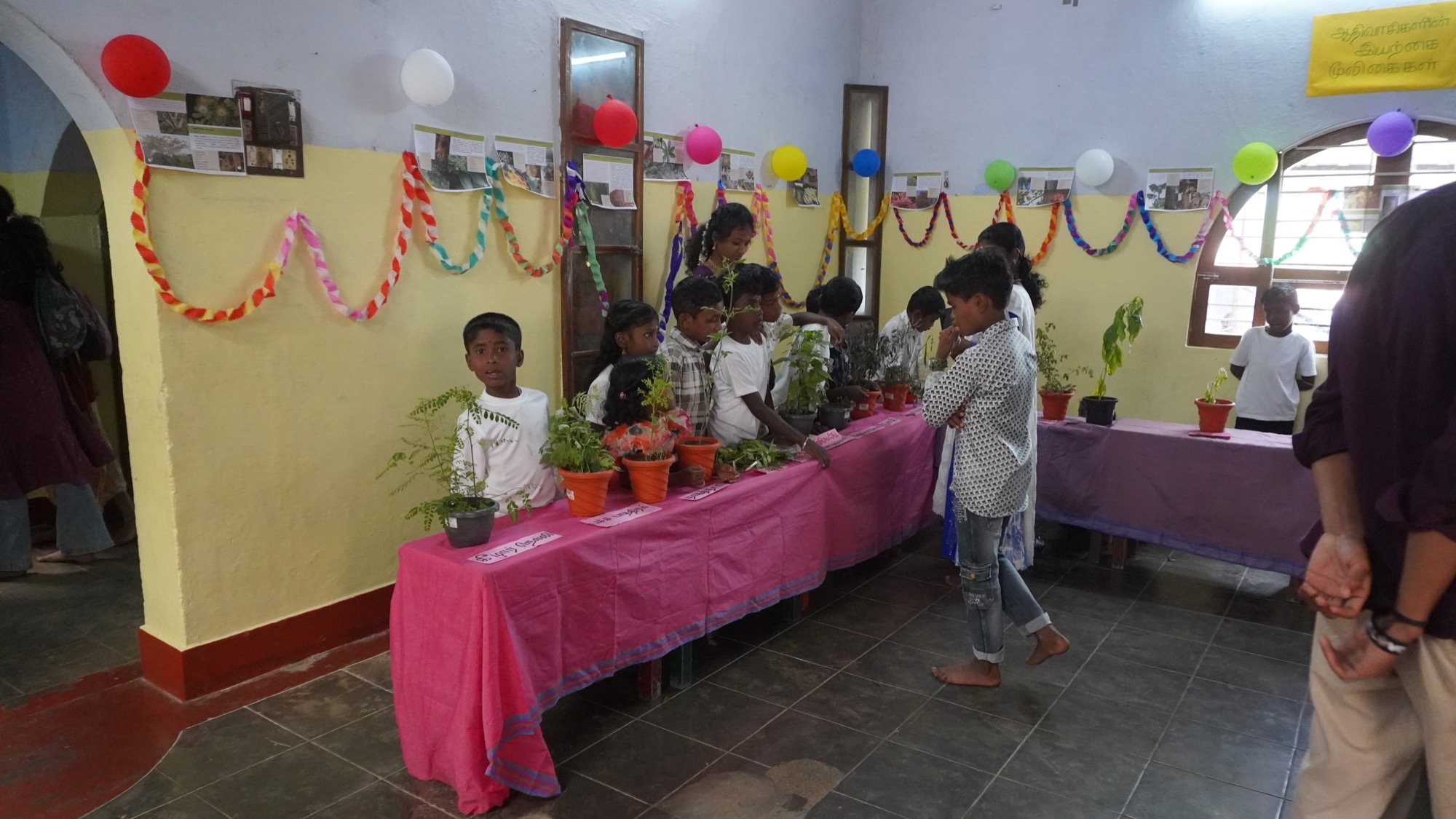Children presenting potted plants and seedlings on decorated tables at an indoor exhibition