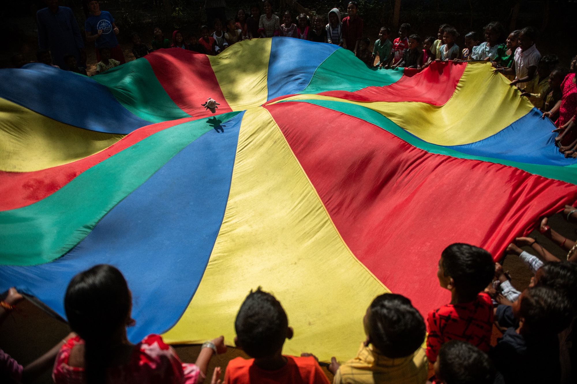 Group of children holding a giant colourful parachute outdoors in a camp activity