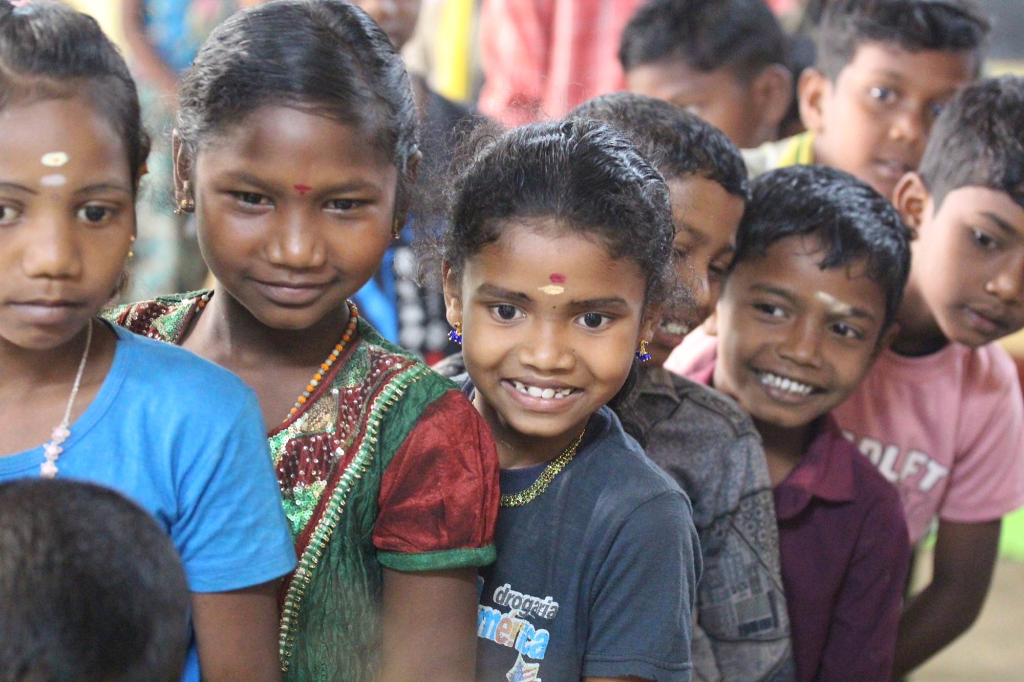Group of smiling Adivasi children lined up, one girl beaming at camera