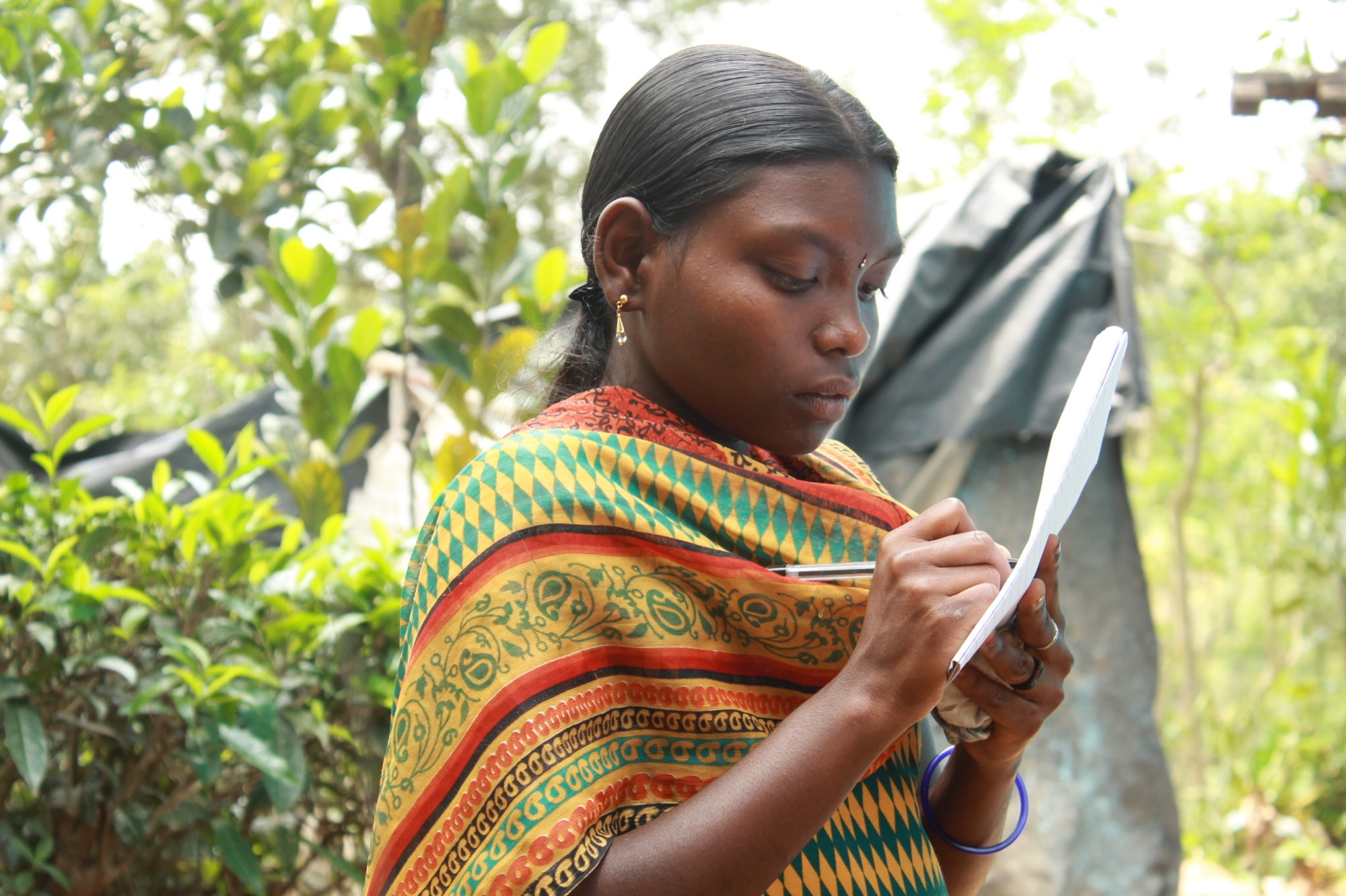Portrait of a young Adivasi woman in a traditional shawl writing notes outdoors
