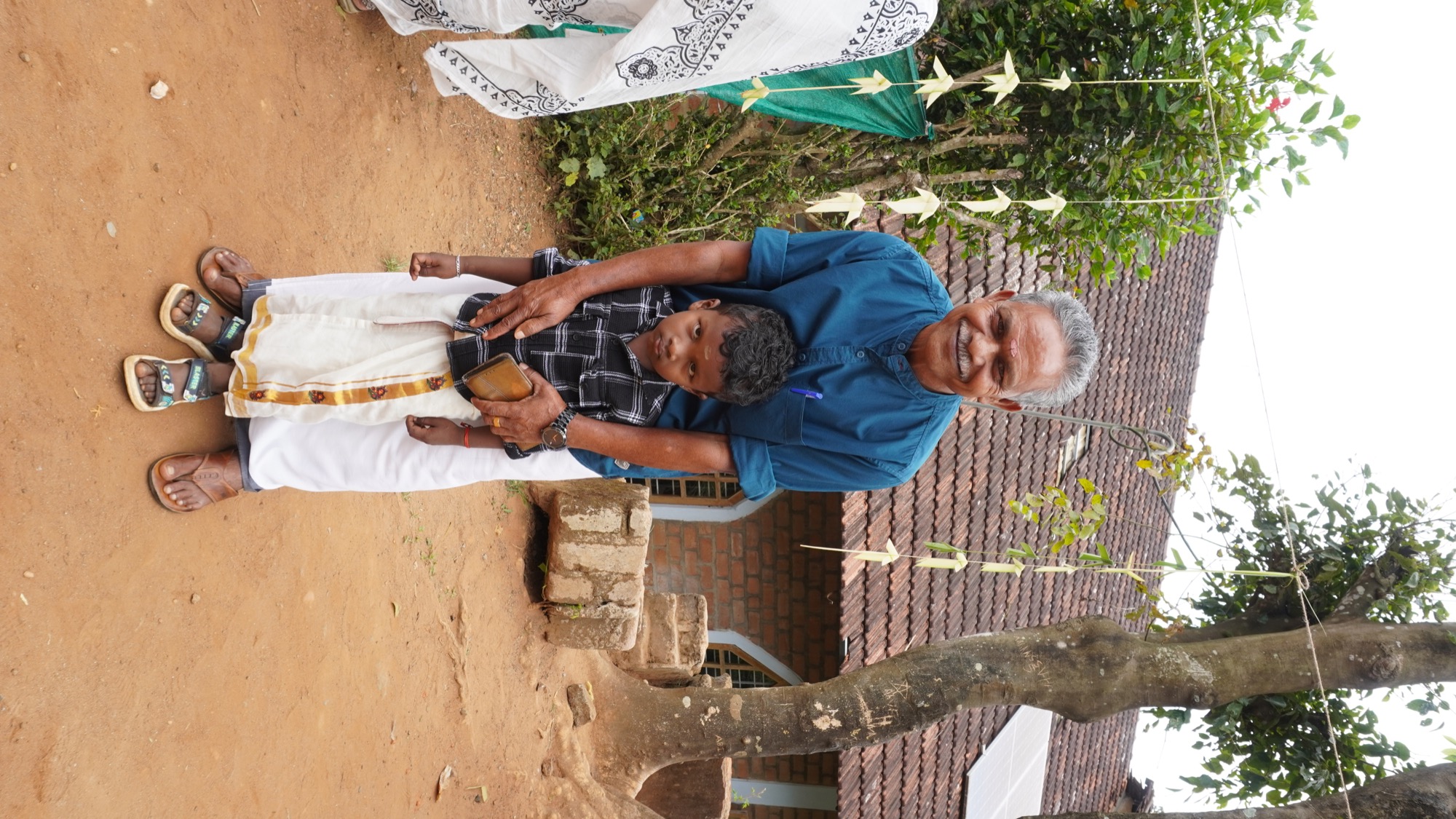 Smiling Adivasi woman in a grey-and-black sari at the community gathering, children walking behind