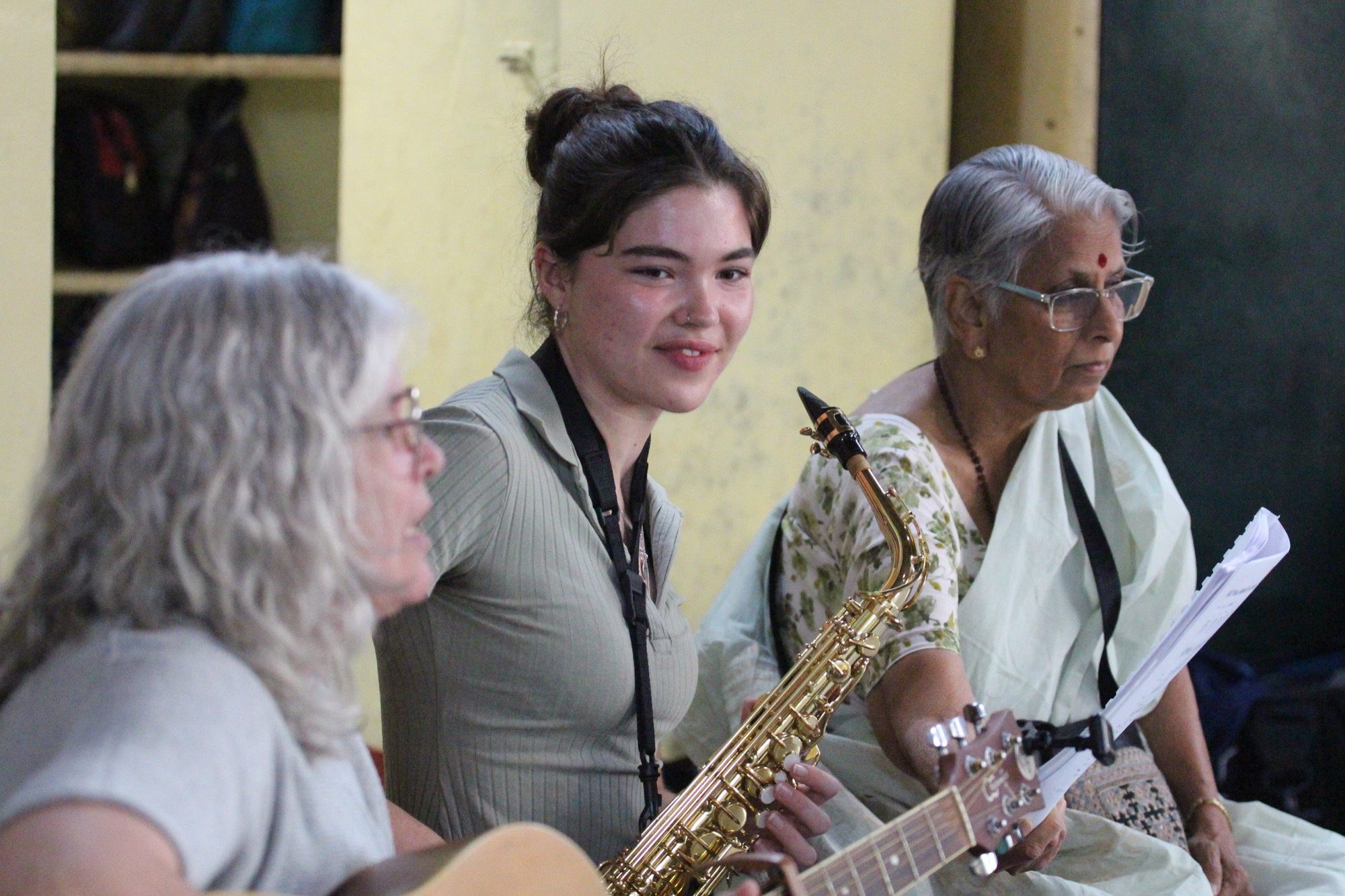 Two visiting musicians (guitar and saxophone) with an elderly woman teacher in a sari, performing together