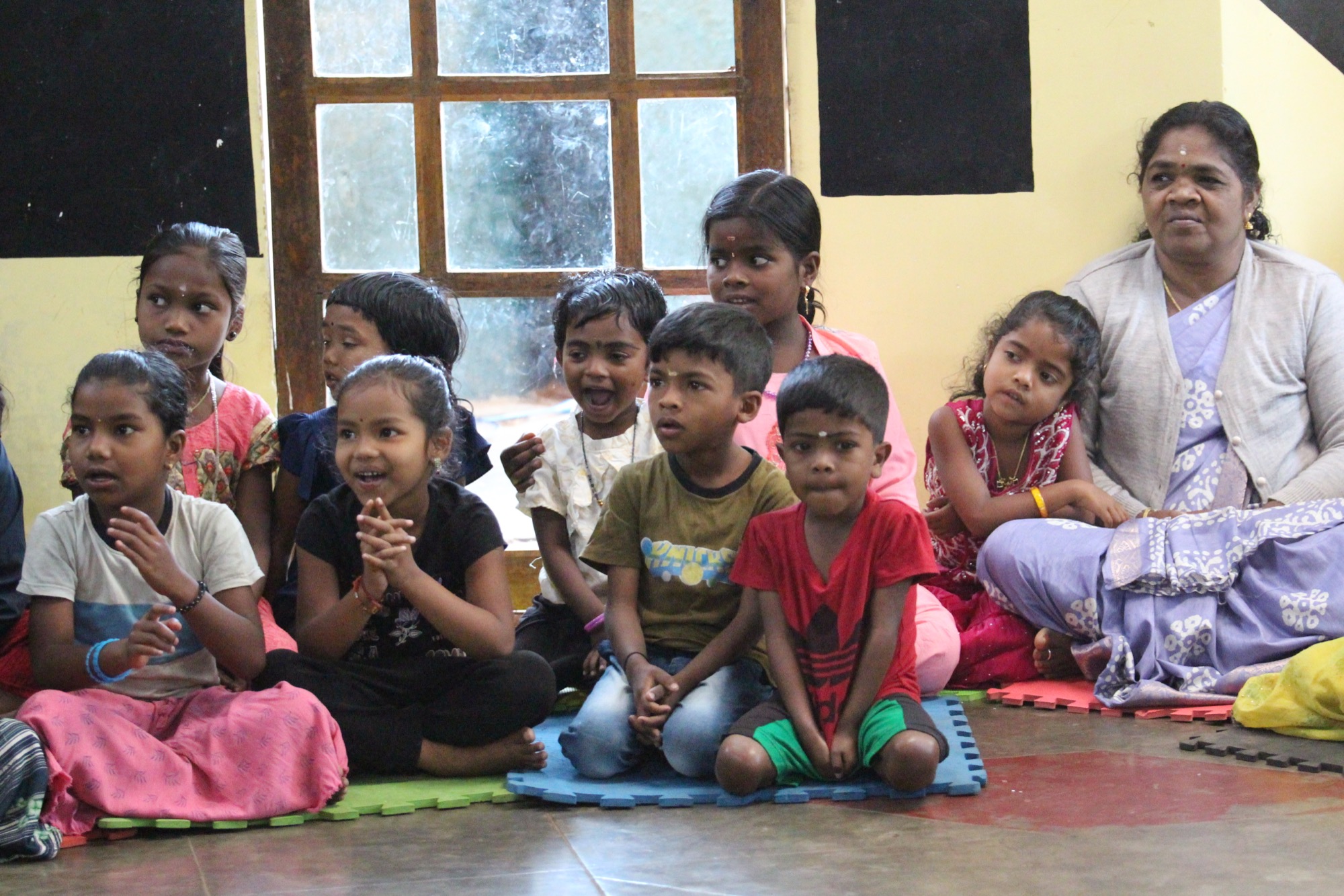 Woman teacher in a cardigan seated among a large group of attentive children
