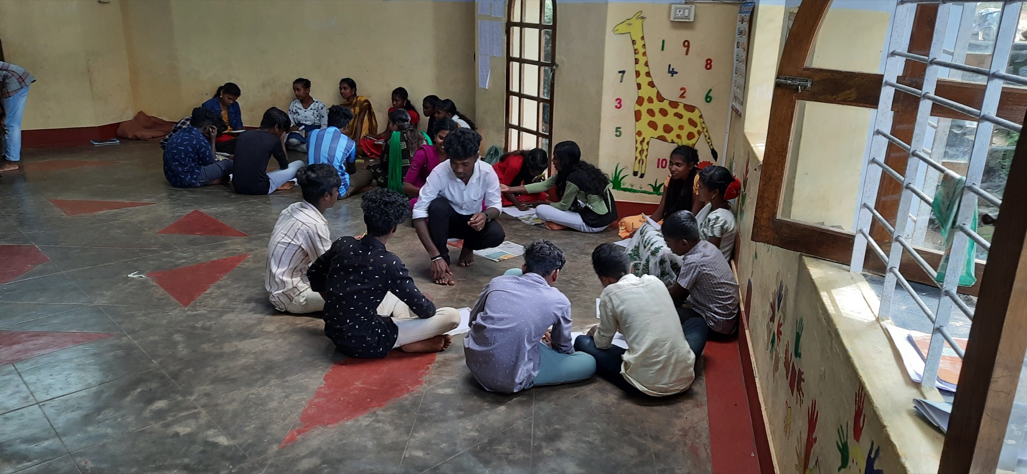 Young people seated on the floor in small groups in a brightly decorated learning centre with a young teacher facilitating
